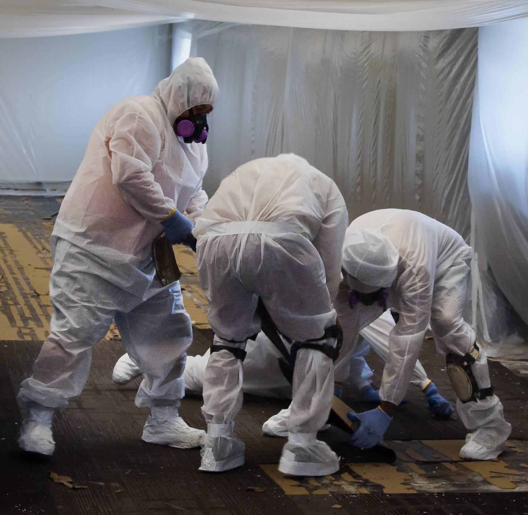 Workers wearing protective gear while they strip the flooring