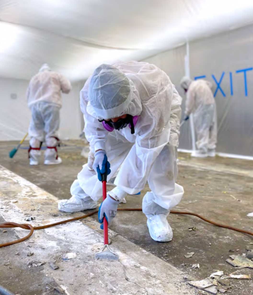 Asbestos abatement team in full protective suits and respirators working in a contained environment to safely remove hazardous materials.
