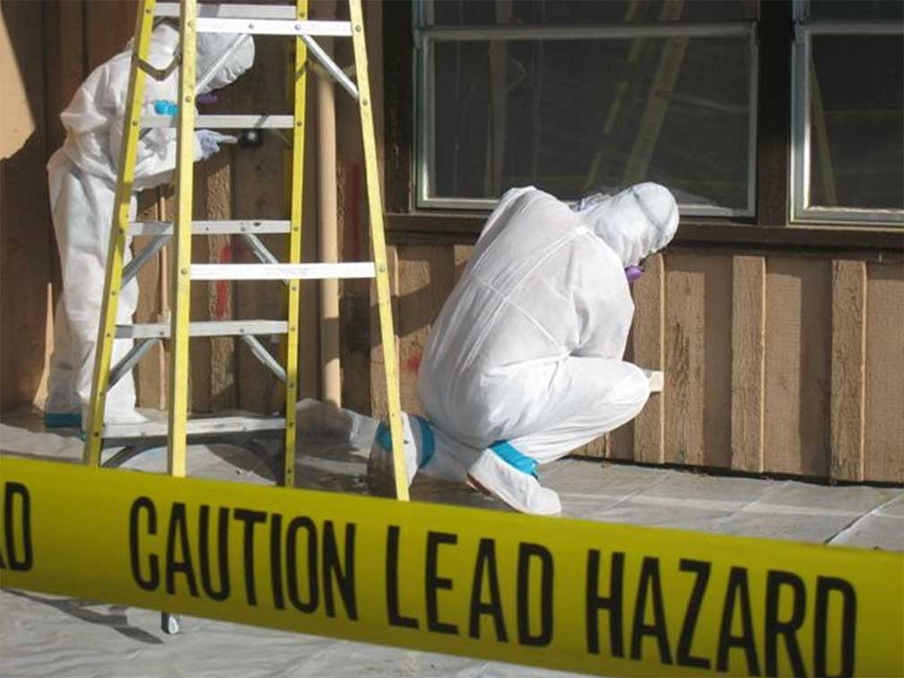 lead_abatement Lead abatement specialists in protective suits removing hazardous lead paint from building exterior with "Caution Lead Hazard" tape